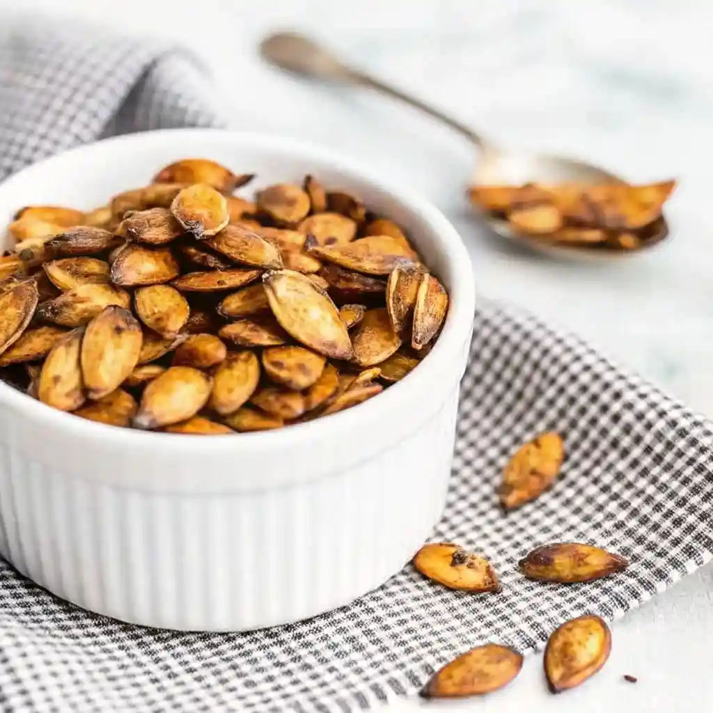 Pumpkin Seed Recipe That Delivers Bold Crunch Fast Pumpkin Seed Recipe Golden roasted pumpkin seeds in a white bowl with scattered seeds and a spoon in the background