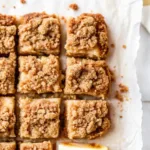 The Ultimate Apple Crisp Bars (Easy & Foolproof Recipe) Apple Crisp Bars Close-up overhead shot of homemade apple crisp bars, cut into a grid of squares on white parchment paper, showing off the golden-brown crumble topping.