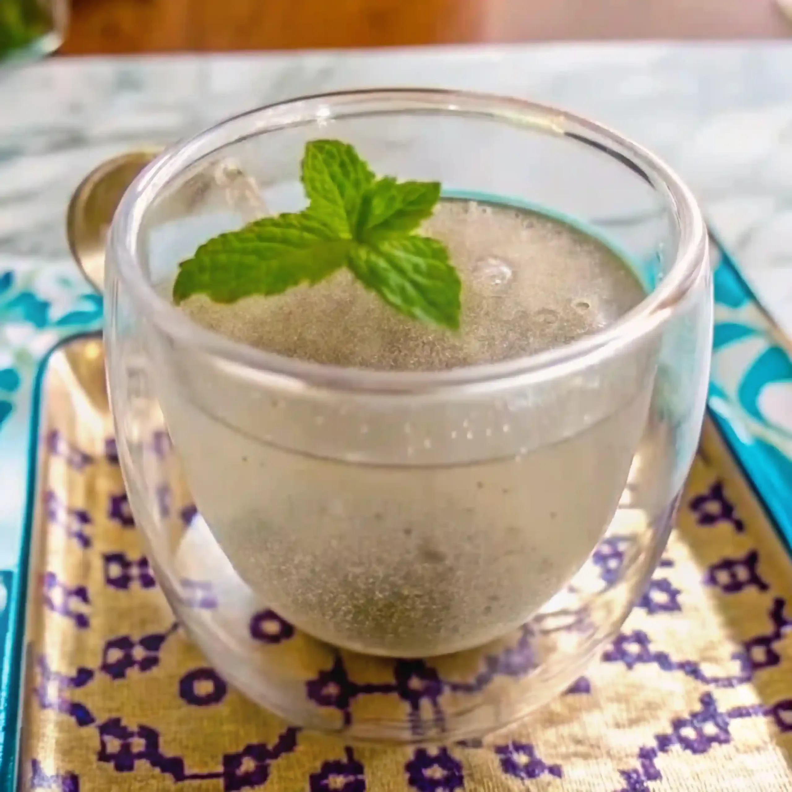 A double-walled glass filled with the bariatric seed drink, garnished with a fresh sprig of mint and sitting on a decorative tray.