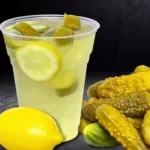 Classic dill pickle lemonade for athletes with lemon slices and pickles in a plastic cup beside whole pickles and a lemon