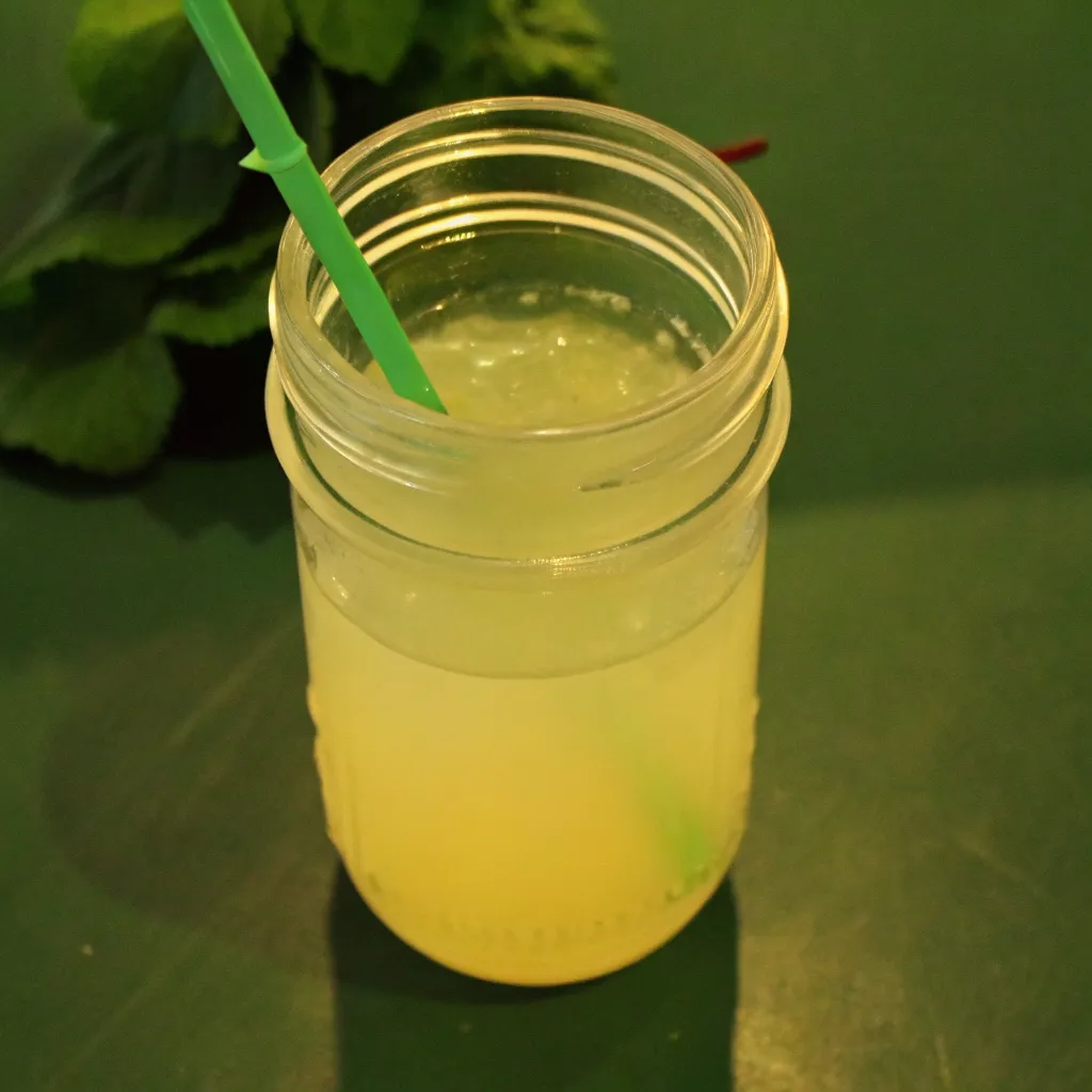Dill Pickle Lemonade Recipe dill pickle lemonade recipe Mason jar filled with dill pickle lemonade and a green straw on a dark green background