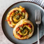 The 5 Best High Protein Pinwheels Recipes high protein pinwheels Two savory high protein breakfast pinwheels served on a dark plate, showing a flaky, golden-brown pastry filled with egg and bacon.