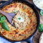 A wooden spoon scooping creamy Marry Me Chicken Dip out of a hot cast-iron skillet, with a cheesy, golden-brown top.