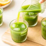 Iced matcha lemonade being poured into a glass with lemon and mint nearby