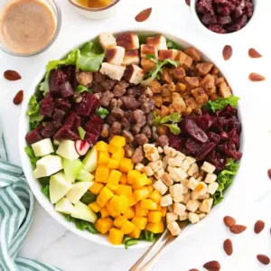 Colorful autumn chopped salad with apples, roasted squash, dried cranberries, nuts, and chicken served in a white bowl.