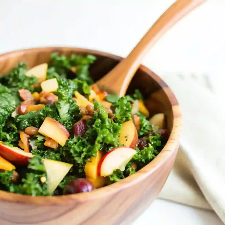Fresh autumn kale salad with apples, grapes, cheddar, and pecans served in a wooden bowl with maple balsamic vinaigrette.