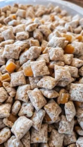 Caramel apple puppy chow coated in powdered sugar with crunchy cereal pieces and chewy caramel bits.
