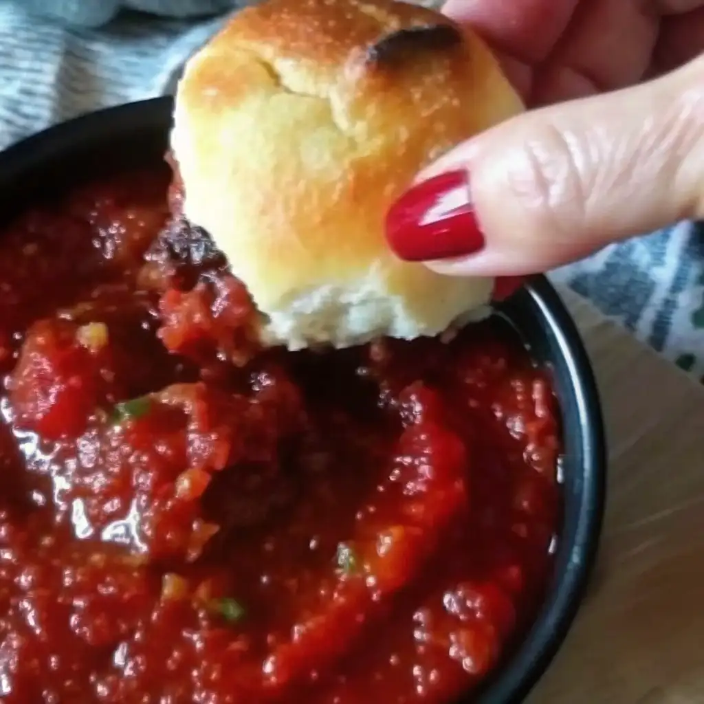 Cheesy Christmas Tree Bread: The Festive Pull-Apart Recipe Everyone Will Love Cheesy Christmas Tree Bread Hand dipping a golden cheesy bread roll into a bowl of chunky marinara sauce.