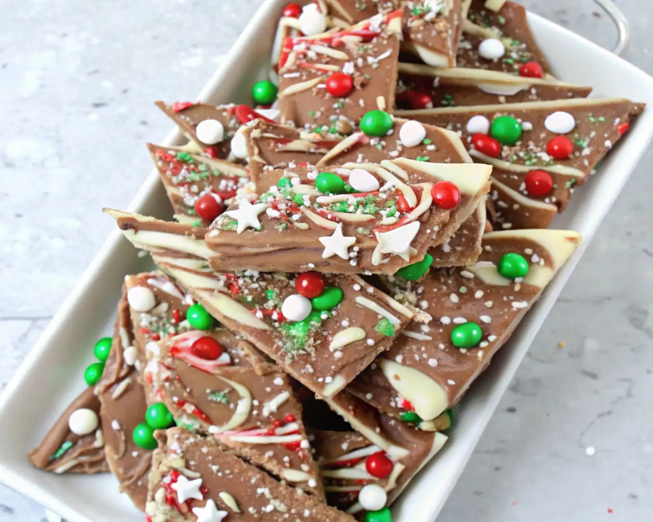 Chocolate candy cane bark topped with red, green, and white candies, peppermint pieces, and white chocolate drizzle