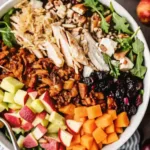 Colorful harvest cobb salad with grilled chicken, roasted squash, apples, dried cranberries, nuts, and fresh greens in a large bowl.