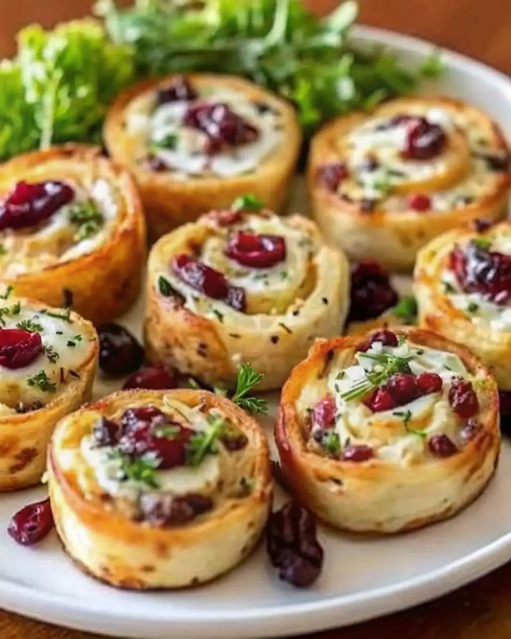 Savory Christmas cranberry roll ups with cream cheese, herbs, and cranberries on a white platter