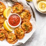Crab stuffed shrimp served with lemon wedges and cocktail sauce on a round plate