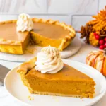 Slice of pumpkin pie with sweetened condensed milk topped with whipped cream on white plate