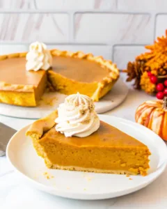 Slice of pumpkin pie with sweetened condensed milk topped with whipped cream on white plate