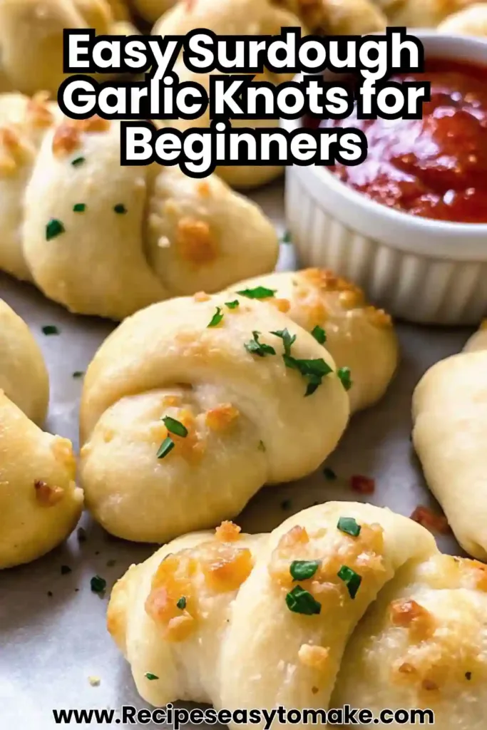 Golden brown sourdough garlic knots on a tray with fresh parsley garnish and tomato dipping sauce.